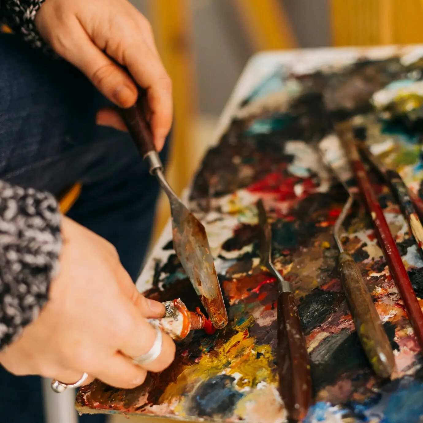 Bildausschnitt von Händen, die mit einem Spachtel Farbe aufnehmen.
